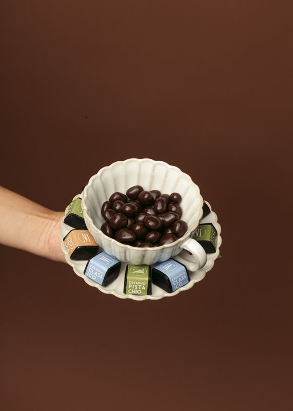 A styled bowl of coffee beans with skincare products against a brown background