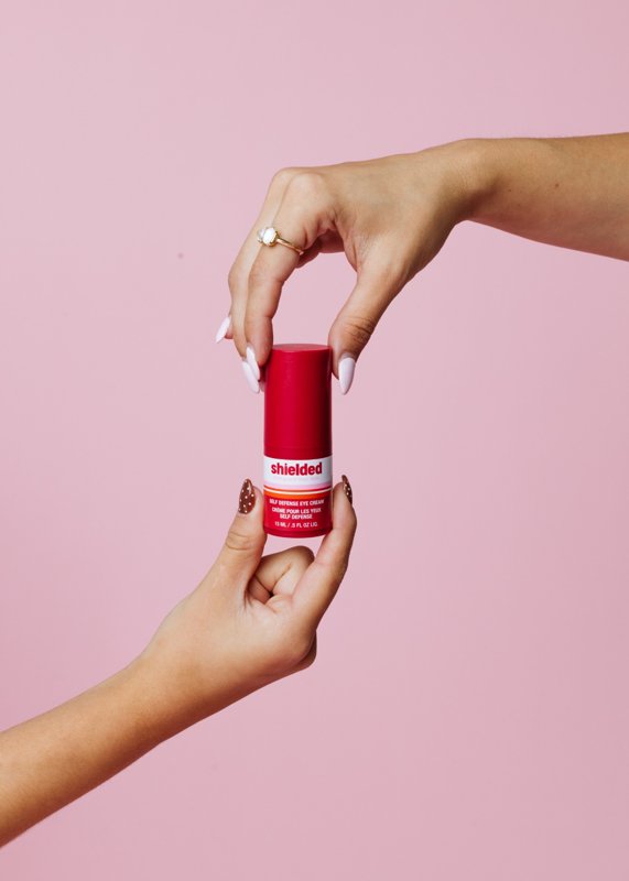 Hands holding a red skincare product against a pink background